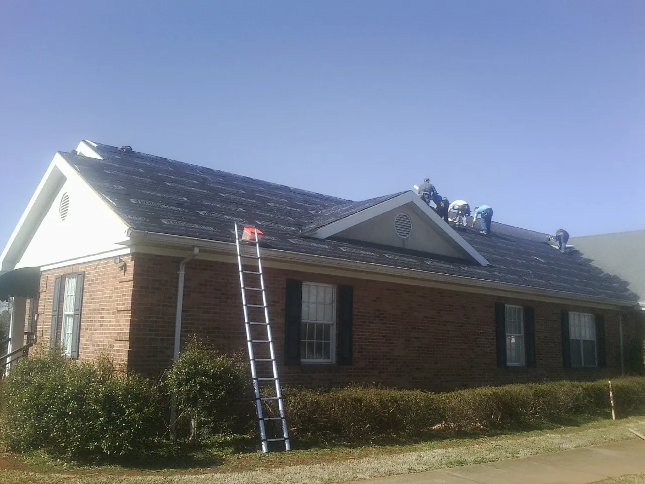 Crew tearing shingles off a brick ranch roof with a ladder set — Metal Roof Repair work by our crew in Blue Creek