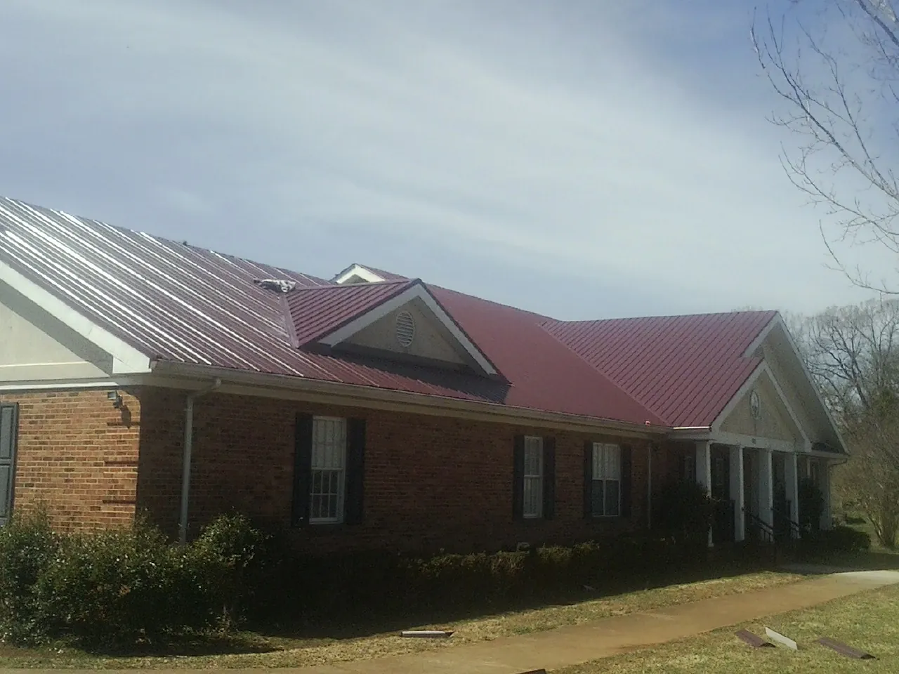 Red metal roof with gabled entries on a long brick building, from a Hail Damage Roof Repair job in Blue Creek
