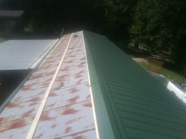 Old rusted panels beside newly installed green metal roofing — Wind Damage Roof Repair by Roofing Brothers in Blue Creek