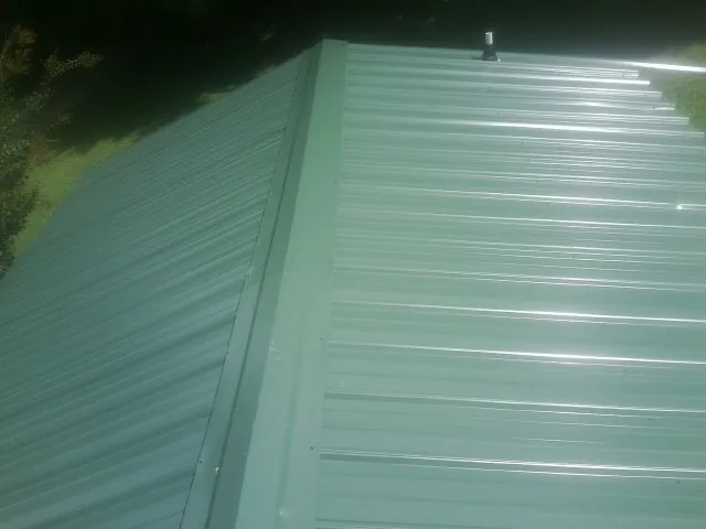 New green metal panels meeting at the ridge of a roof — Flat Roof Repair work by our crew in Blue Creek
