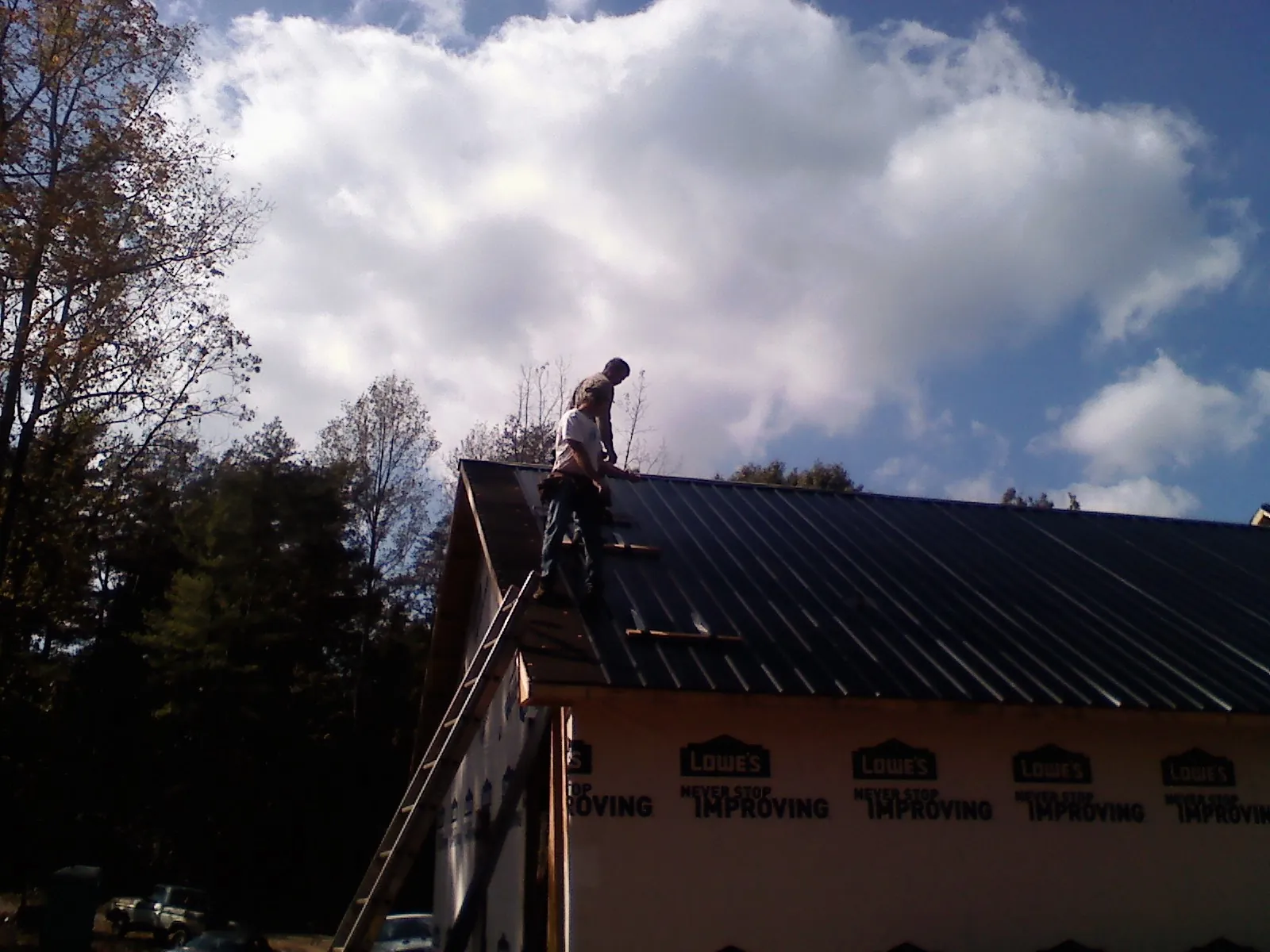 Roofer fastening dark metal panels high against a cloudy sky, from a Roof Inspection job in Blue Creek