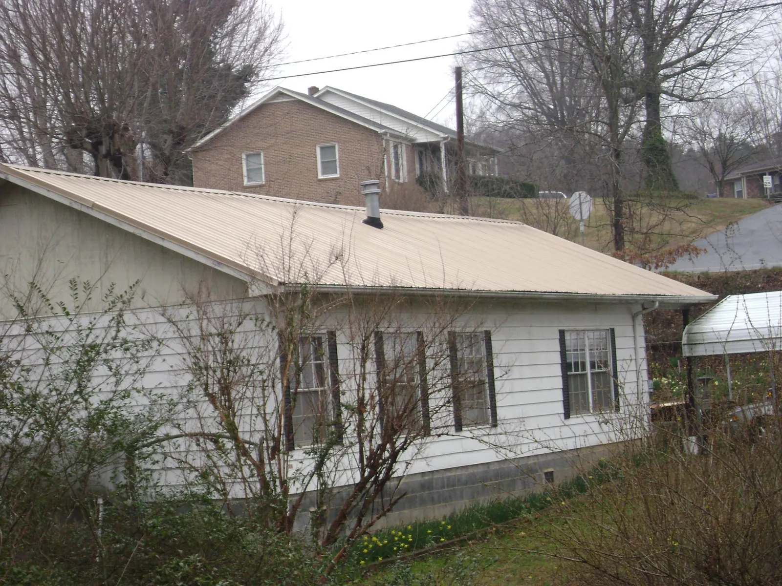 Tan metal roof on a white sided house set into a hillside — Commercial Roofing by Roofing Brothers in Blue Creek