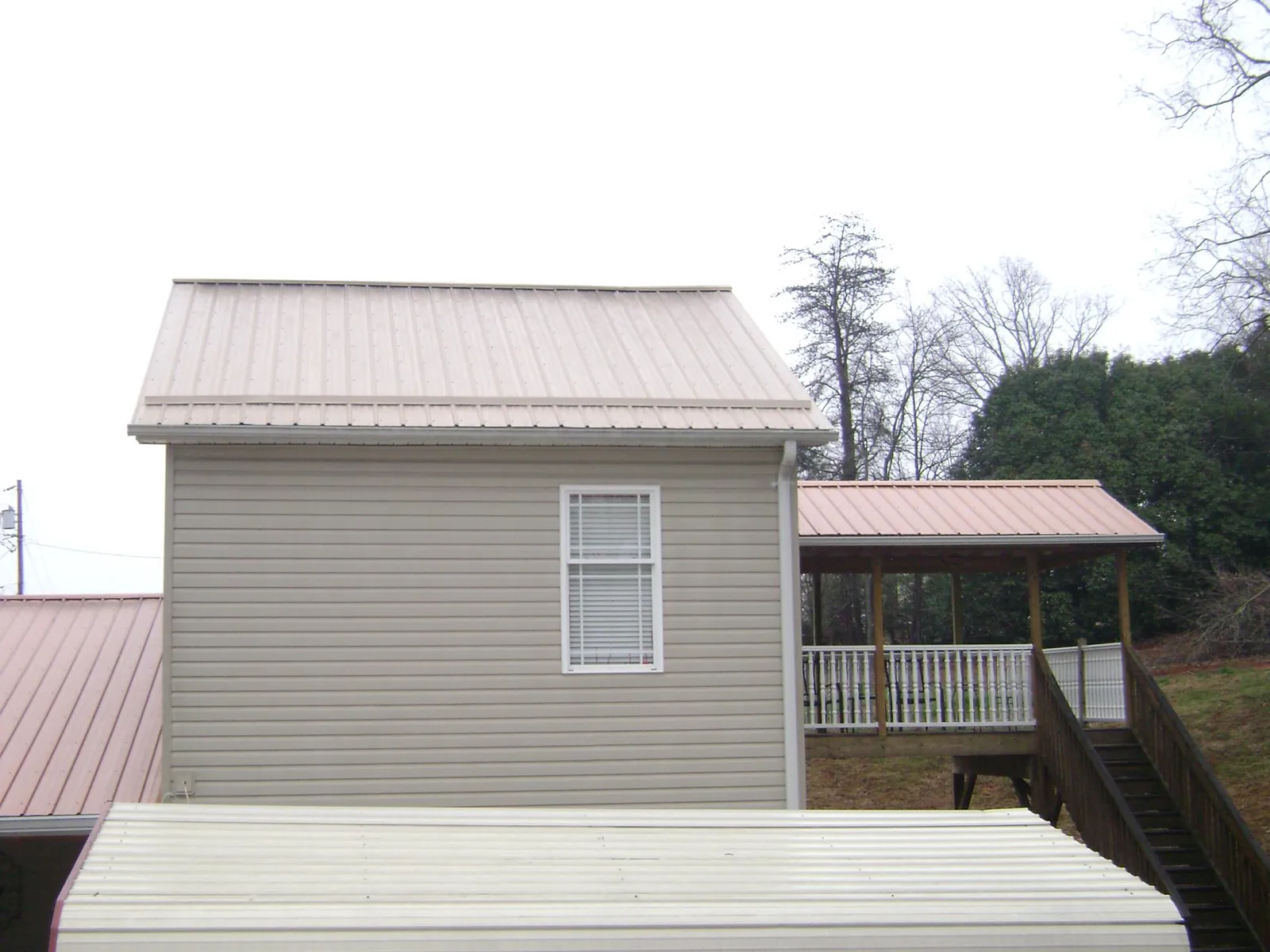 Tan metal roofs on a two story addition and attached porch, from a Roof Replacement job in Blue Creek